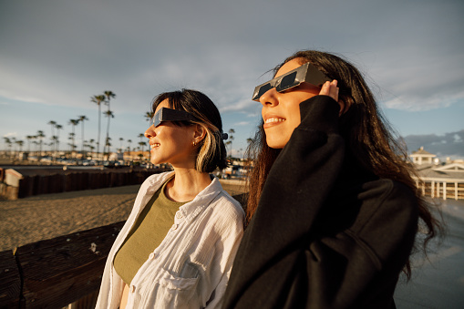 Two friends have fun together during a solar eclipse event. Their looking and pointing to the sun wearing the typical glasses normally used to watch a solar eclipse.