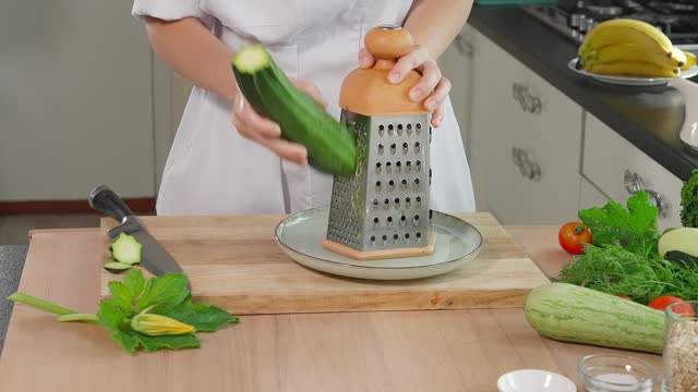 Chef preparing a healthy dish, grating green zucchini on a fine grater, wooden background. Healthy eating concept, vegetarian food, vegetables rich in vitamins, diet. Close-up, front view