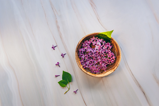 Spa and wellness composition with perfumed lilac flowers water in wooden bowl on marble background. Aromatherapy, top view.