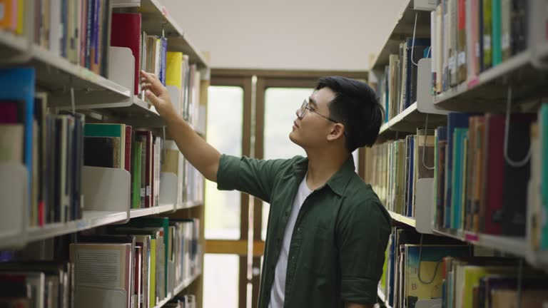 Young man spending his free time browsing through books from the shelves in the library