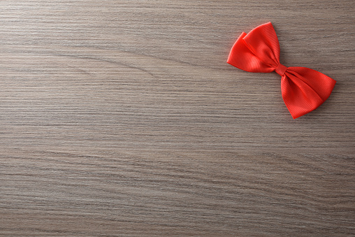 Little red bow at the top right for event background decoration on wooden table. Top view.
