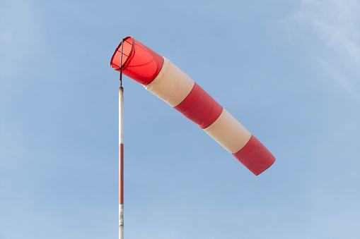 Gray steel sky with red airsock and signal light for wind direction at storm in airports, ports, meteostation and weather forecast