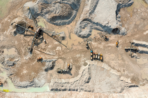 Aerial view of a stone crusher maschine, conveyor belts, bulldozers, dump trucks and heaps of excavated stone and sand in a quarry site.