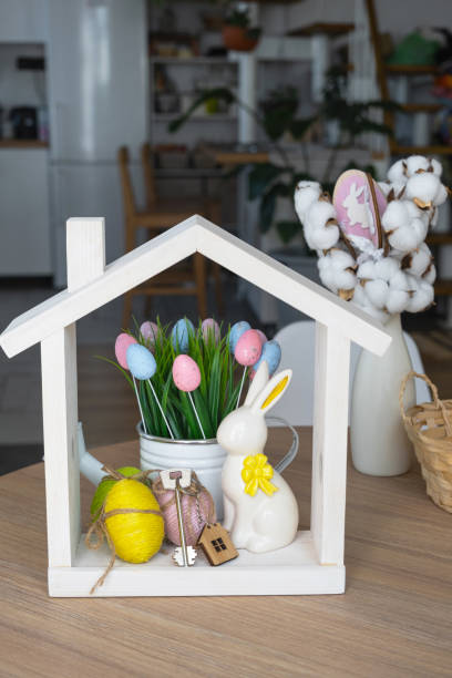 istock Key and tiny house of cozy home with Easter decor with rabbit and eggs on table of kitchen. Building, design, project, moving to new house, mortgage, insurance, rent and purchase real estate 2116817276