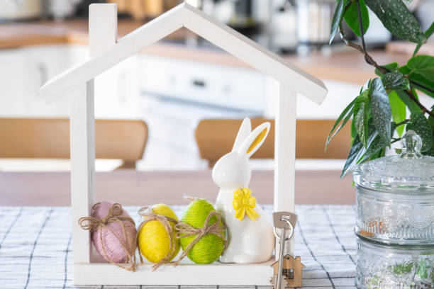 istock Key and tiny house of cozy home with Easter decor with rabbit and eggs on table of kitchen. Building, design, project, moving to new house, mortgage, insurance, rent and purchase real estate 2116817277