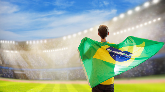 Brazil football supporter on stadium. Brazilian fans on soccer pitch watching team play. Group of supporters with flag and national jersey cheering for Brazil. Championship game.