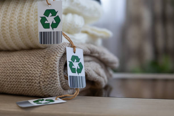 istock A stack of knitted clothes made from natural wool. Biodegradable, eco-friendly natural clothing with green arrow recycling label, folded into a neat stack. Natural eco-friendly clothing. 2116834036