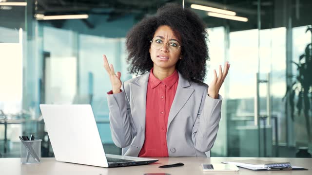 Frustrated young african american businesswoman complains about poor performance of software on laptop sitting in office.