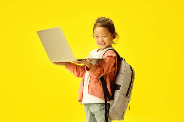 istock Cheerful Asian Child with Laptop and Backpack on Sunny Yellow 2116840921