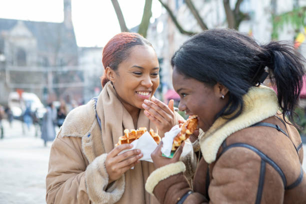 dos mujeres jóvenes comiendo gofres en bruselas - brussels waffle belgian waffle people fotografías e imágenes de stock