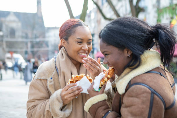 two young women eating waffles in brussels - brussels waffle belgian waffle people imagens e fotografias de stock