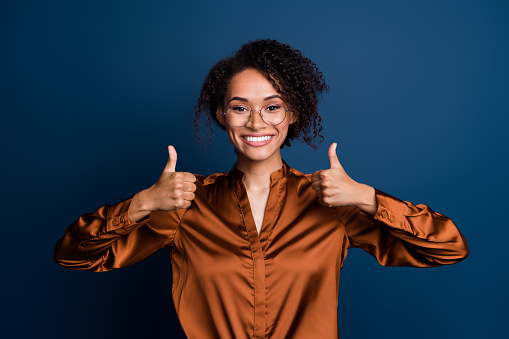 Photo of adorable cool woman dressed brown silk shirt eyewear showing two thumbs up isolated blue color background.