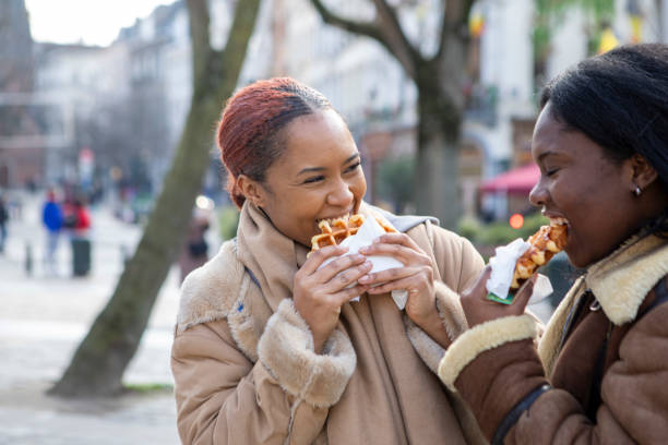 two young women eating waffles in brussels - brussels waffle belgian waffle people fotografías e imágenes de stock