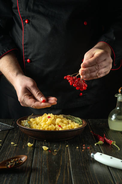 Adding viburnum berries in a cook hand to a plate of pasta. The chef at the kitchen table in the tavern is preparing a delicious lunch