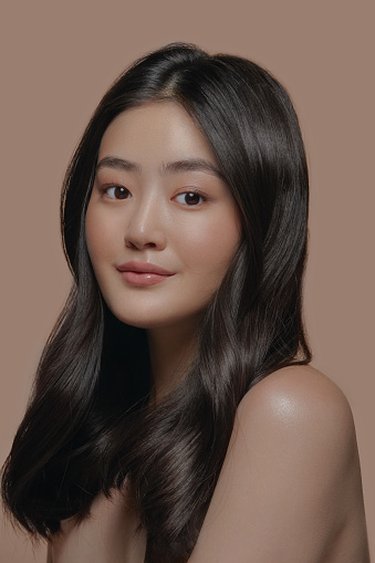 Vertical shot of beautiful young Asian woman with clean fresh skin on a beige background. Facials, Cosmetology, Beauty and Spa, Portrait of Asian women.