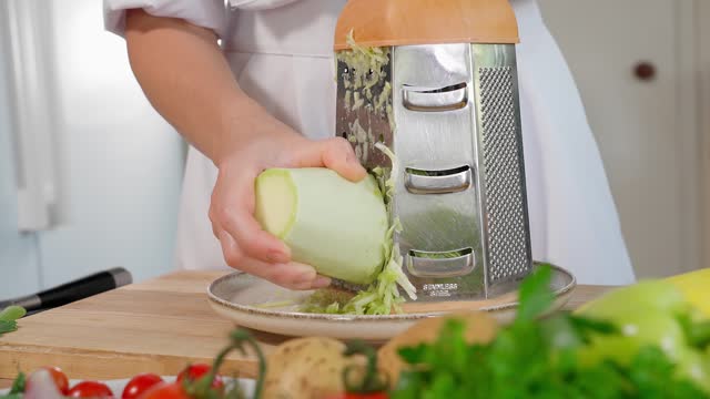 The chef is preparing a healthy dish, grating white zucchini on a coarse grater, with vegetables in the background. Healthy eating concept, vegetarian food, vegetables rich in vitamins, diet. Close-up