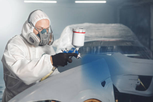 istock Car paint worker spraying blue paint to car body element using spray gun in vehicle workshop chamber. Complex restoration of automobile body. 2116871023