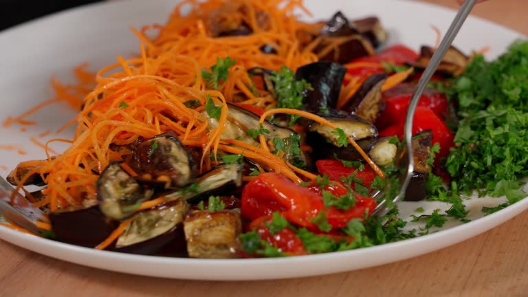 A salad of roasted eggplant, red peppers, fresh carrots and herbs combines the sauce with the vegetables. Macro, front view. Snack, food, vegetables, vegetable salad, eggplant dishes.