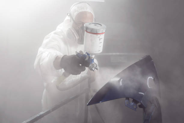 istock Professional bodywork, male car painter in protective mask and workwear apply few layer lacquer from spray gun to automobile body parts in garage booth. 2116874775