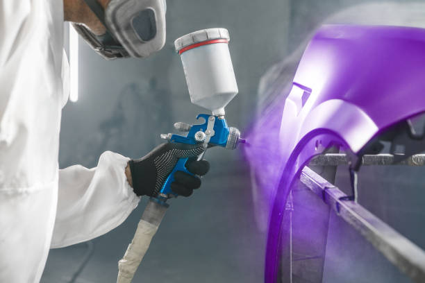 istock Car paint worker spraying purple paint to car body element using spray gun in vehicle workshop chamber. Complex restoration of automobile body. 2116875302