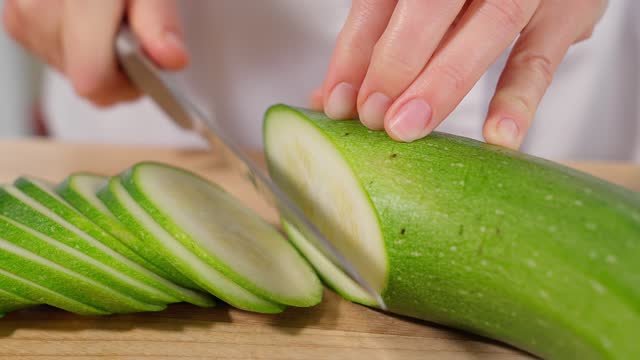 The chef cuts green zucchini into slices with a knife, preparing a healthy meal. Healthy eating concept, vegetarian food, vegetables. Close-up, front view, macro