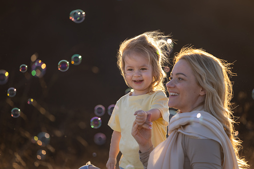 Happy mother and her little daughter play with bubbles in nature