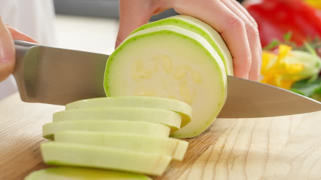 A girl cuts white zucchini into slices on a wooden board. Healthy eating concept, vegetarian food, rich in vitamins, diet, vegetables. Close-up, front view.