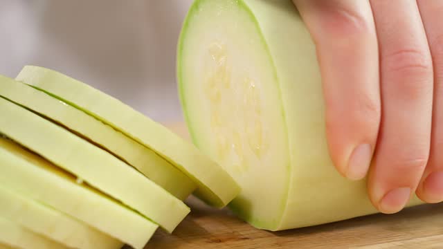 The chef cuts white zucchini into slices on a wooden board. Healthy eating concept, vegetarian food, rich in vitamins, diet, vegetables. Close-up, front view, macro