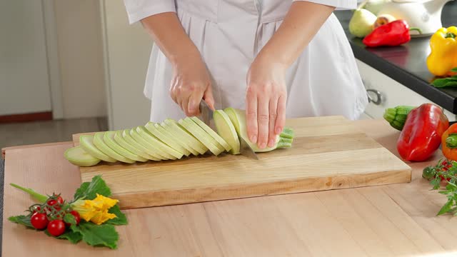 The chef cuts white zucchini into slices on a wooden board, with vegetables in the background. Healthy eating concept, vegetarian food, rich in vitamins, diet, vegetables. Close-up, front view.