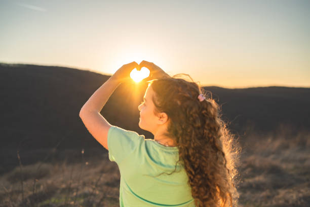 Teenage girl hands making heart shape around the sun