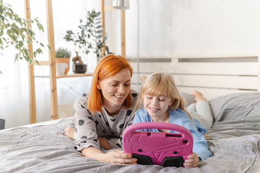 Photo of a beautiful mother and her little daughter enjoying in bed and using digital tablet