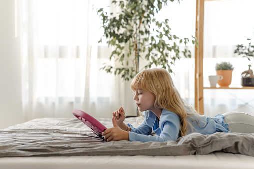 Shot of a cute little girl with blonde hair enjoying in bed and using digital tablet