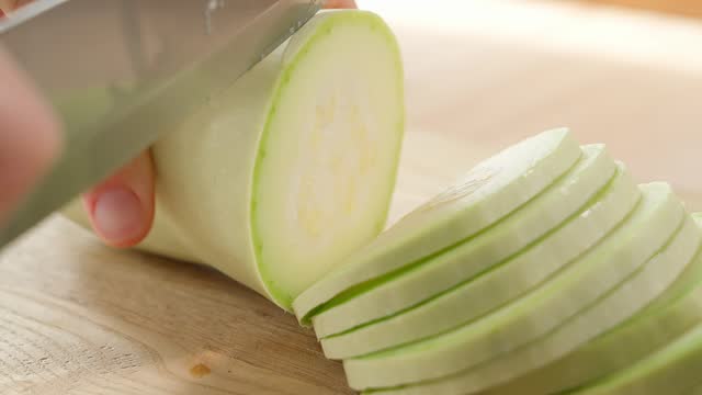 A girl cuts white zucchini into slices on a wooden board. Healthy eating concept, vegetarian food, rich in vitamins, diet, vegetables. Close-up, side view, macro