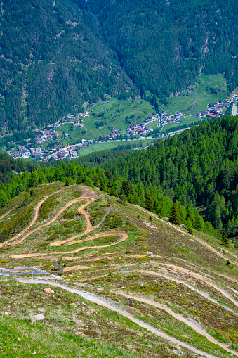 Downhill track widing down the mountain in the Ötztal Arena ski area in TIrol in the Austrian Alps during a beautiful springtime day. Mountainbikers are going up the mountain in the ski lifts and cycling down on various tracks towards the valley.