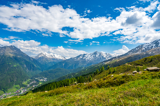 View over the Ötztal from the Ötztal Arena ski area in TIrol in the Austrian Alps during a beautiful springtime day. Sunlight is hitting the valley below while there are some clouds over the snow covered mountain peaks in the background.