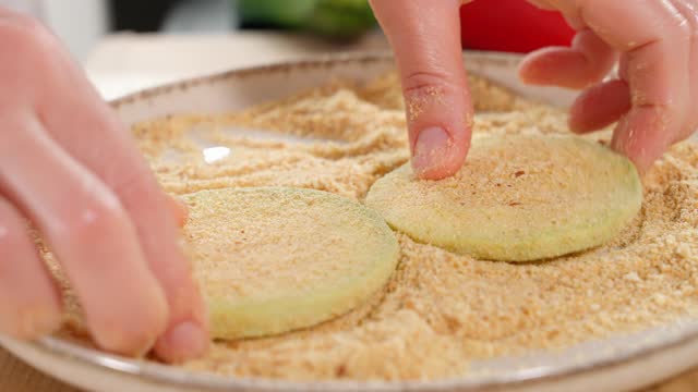 The chef sprinkles slices of white zucchini in breadcrumbs. Zucchini dish, zucchini recipe, vegetarian food, quick snack, party. Macro, side view