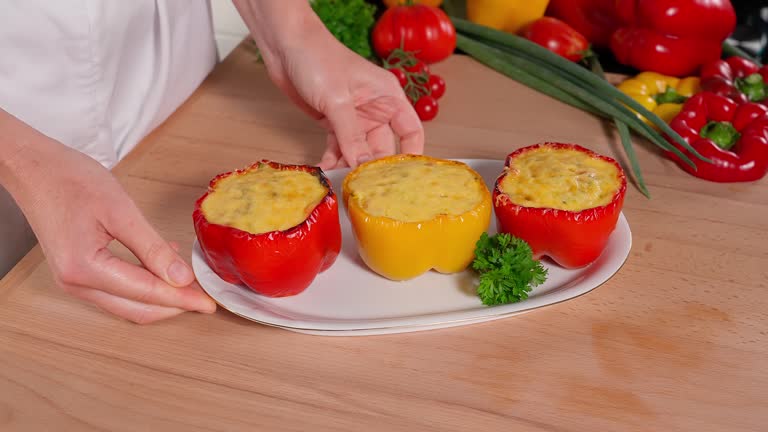 Baked stuffed red and yellow peppers with a mixture of eggs and vegetables with cheese on a white plate, on a wooden table on a background of vegetables. Healthy eating concept. Close-up