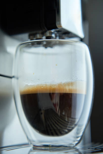 Fresh espresso in clear glass at morning. Coffee machine on dark background, close up. Modern coffee maker with freshly brewed coffee in glass cup. Kitchen appliances
