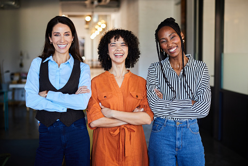 A multi-ethnic group of female business professionals are standing together in a group and are smiling while looking at the camera.