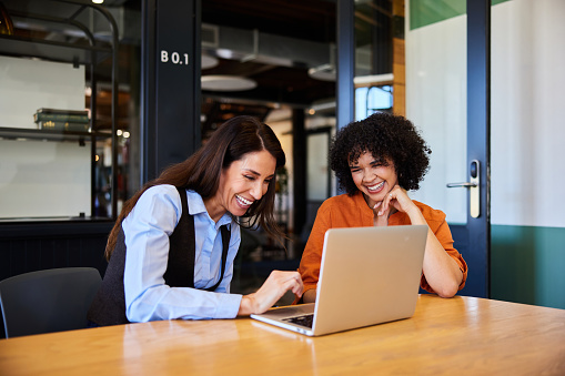 Diverse businesswomen laughing over a laptop while working in an office