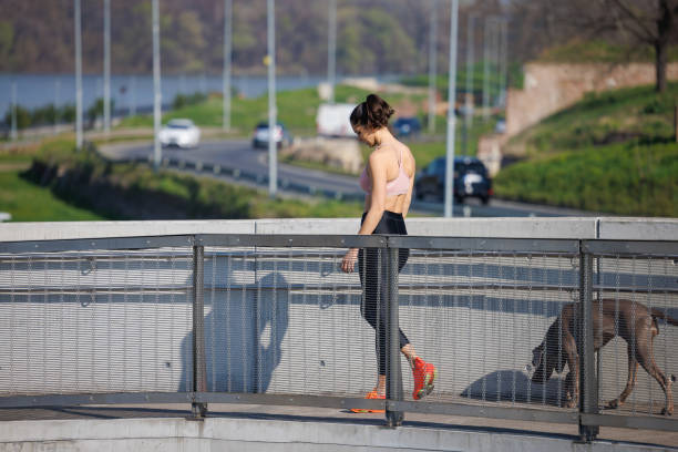 Active young woman walking with her dog on elevated walkway after running on a fine day, preparing for marathon
