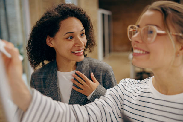 istock Smiling young businesswomen is writing something on whiteboard in office 2116975416
