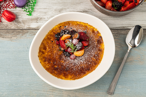Creme brulee decorated with fruits and powdered sugar on a wooden table