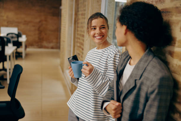 Smiling diverse female employees is talking and drink coffee during break time in stylish office