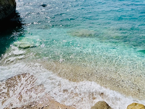 Rocky beach and crystal turquoise water of Ionian Sea in Albania. Calm and relaxing view with flowers. summer holidays concept background. Copy space. Horizontal photo.