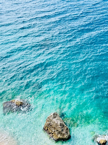 Rocky beach and crystal turquoise water of Ionian Sea in Albania. Calm and relaxing view with flowers. summer holidays concept background. Copy space. Vertical photo.