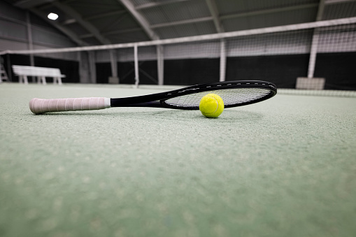 Tennis ball under racquet in sports court.