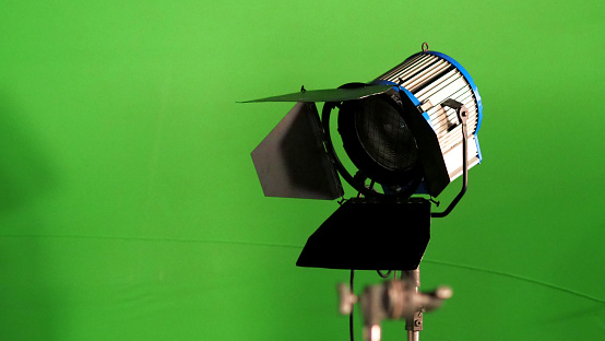 Big studio LED spotlight for video movie or photo film production with green screen background for chroma key technique in post lab process and professional equipment such as tripod and others.