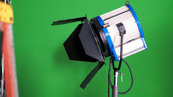 Big studio LED spotlight for video movie or photo film production with green screen background for chroma key technique in post lab process and professional equipment such as tripod and others.