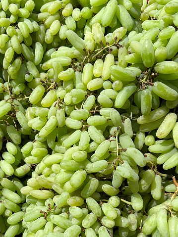 Stock photo showing close-up, elevated view of a large heap of white seedless grapes displayed on an outdoor market stall.